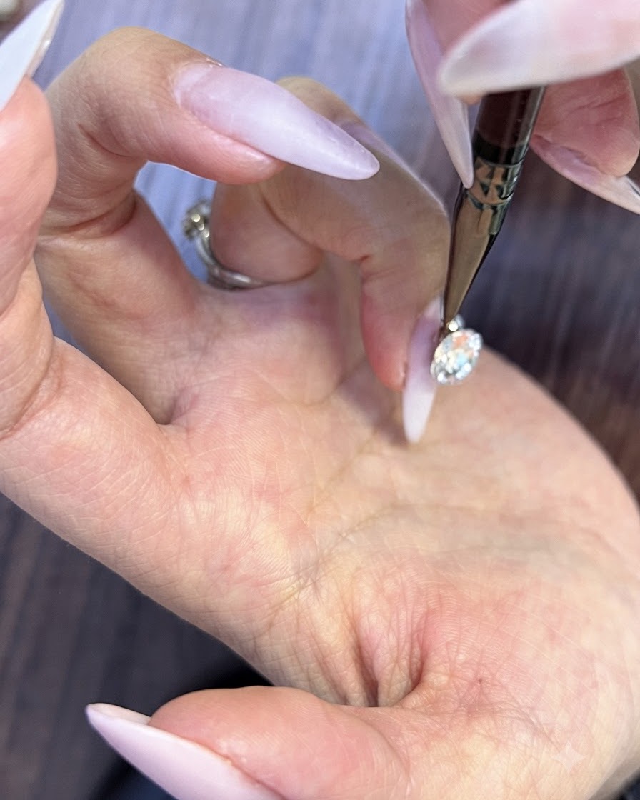 細いディテールツールを使って、大きなネイルクリスタルの下の小さな隙間に微小な丸いラインストーンを配置している様子。