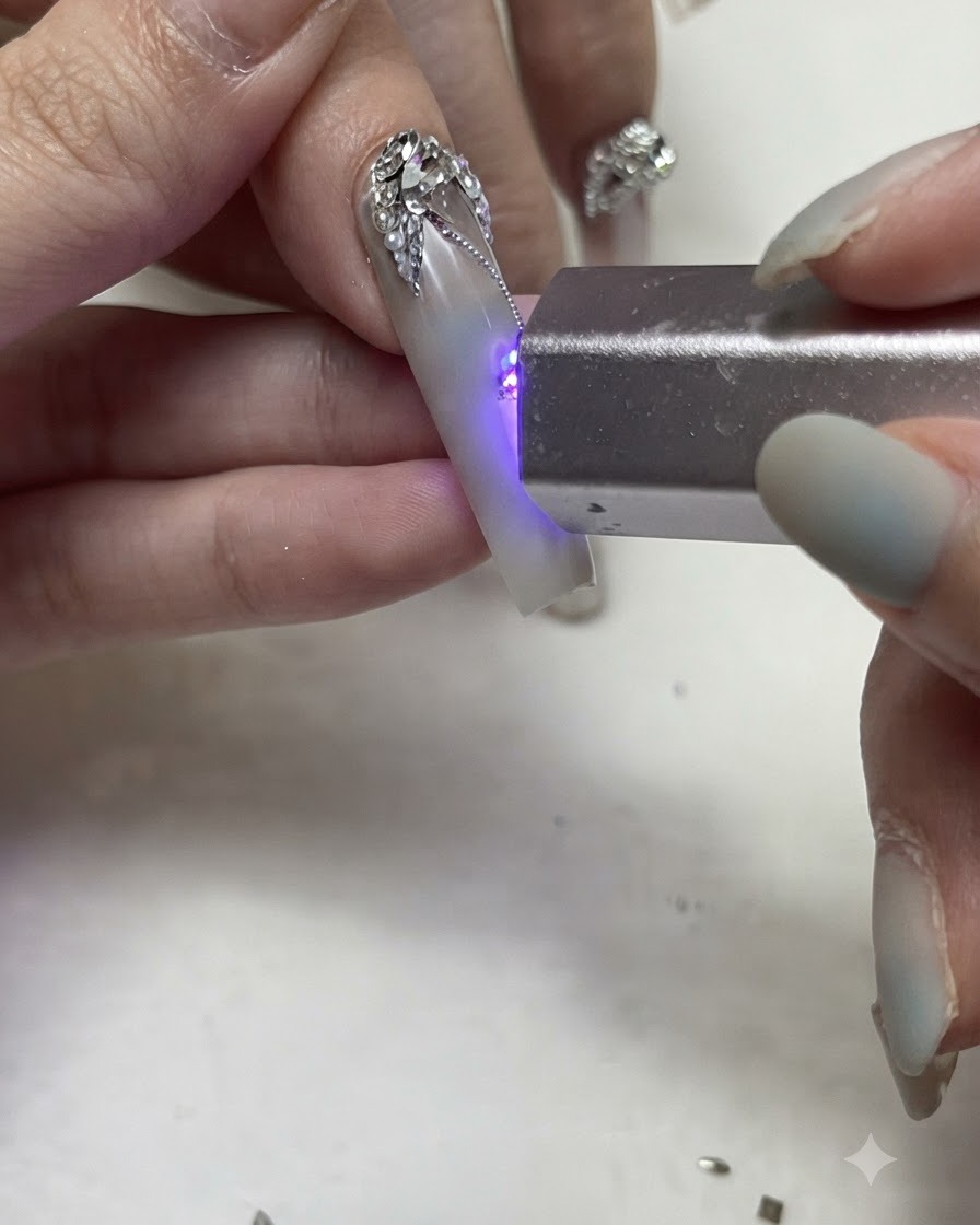 ポータブルなUV/LEDフラッシュライトが、装飾されたネイル上の細かいシルバージェルのラインとラインストーンのディテールを硬化させている様子。