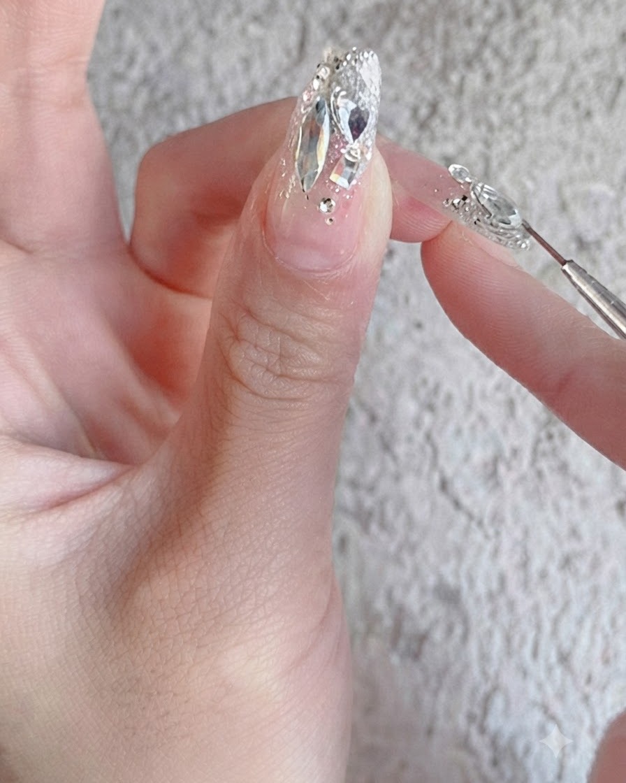 完全に仕上がったラインストーンネイルデザインの上に、ツヤのある補強用トップコートをネイルブラシで塗る様子