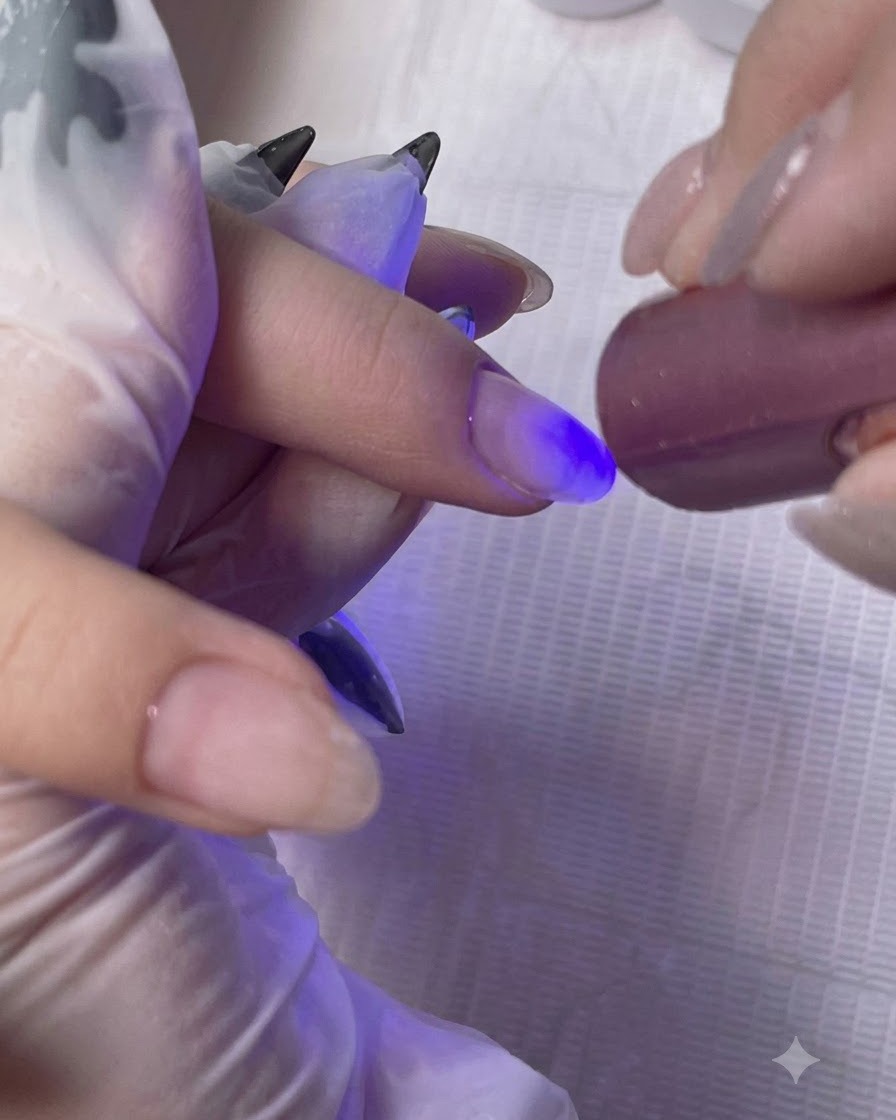 持ち運び用のミニUV・LEDランプで、クライアントの指に塗布したベースコート層を硬化させている様子。