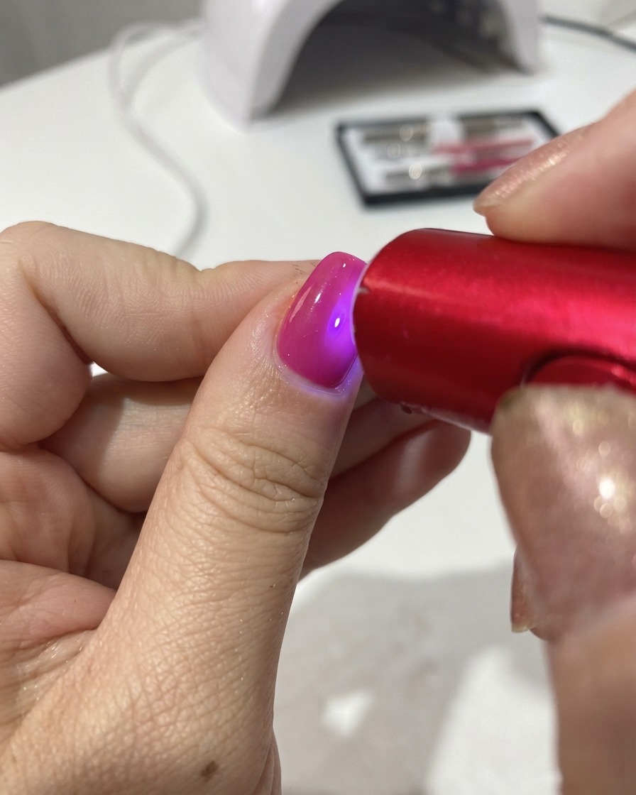ポータブルな赤いUV/LEDランプが爪の上のジェルポリッシュを硬化させているところ。