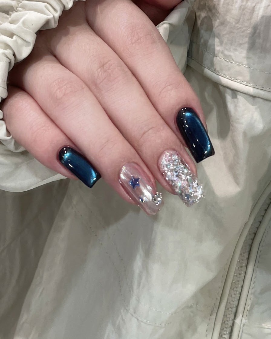ディープブルーのキャッツアイネイルの横に、星の装飾が施されたアクセントネイルとフルグリッターネイルがある仕上がりの手。