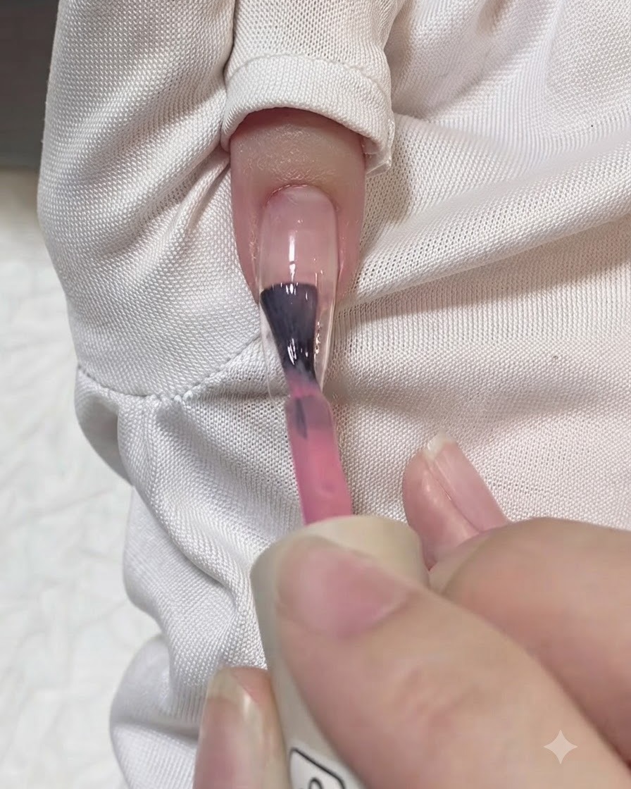 クリアネイルエクステンションの中心に半透明ピンクジェルのストロークを筆で塗布している様子。