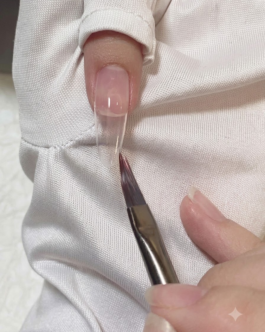 フラットブラシで爪の上のピンクジェルの端をなめらかに整えてぼかしている様子。
