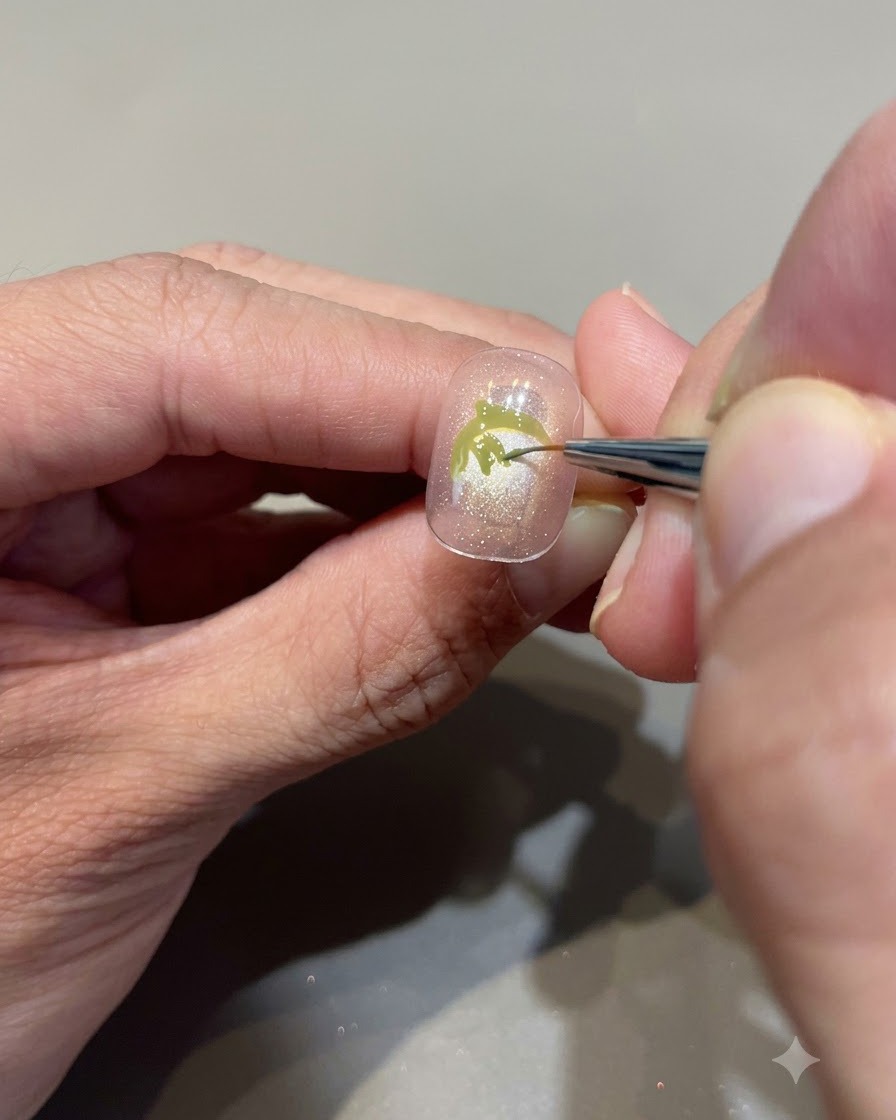 ヌードピンクのネイル上にイチゴの葉を作るため、アボカドグリーンのジェルを細いディテールブラシで緻密に塗りつぶしているクローズアップ画像。