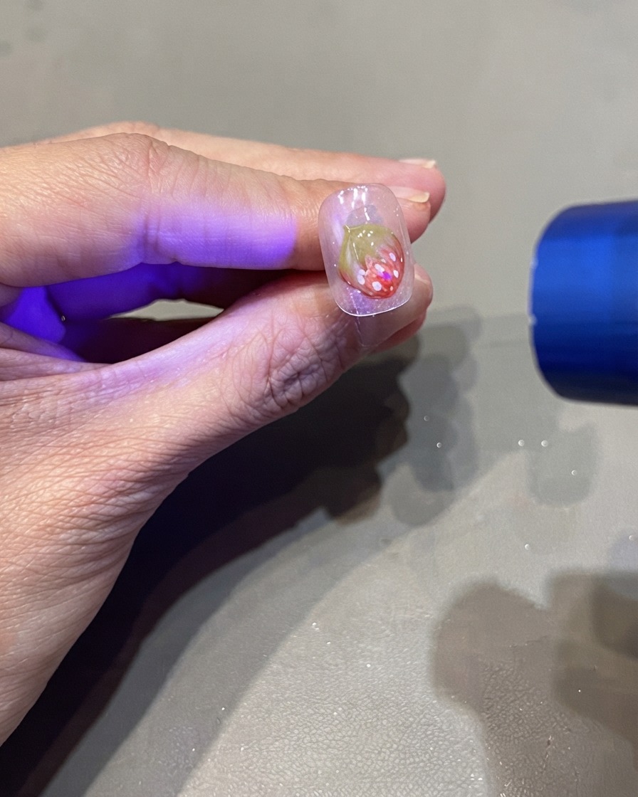ポータブルUVフラッシュライトで3Dイチゴネイルのデザインを硬化させている様子。