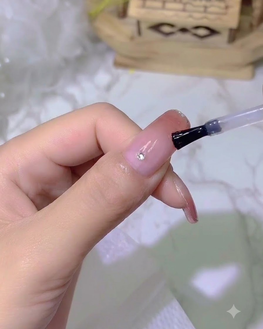 専用の細いツールを使って、小さな輝くクリスタルを爪の上に乗せている様子。