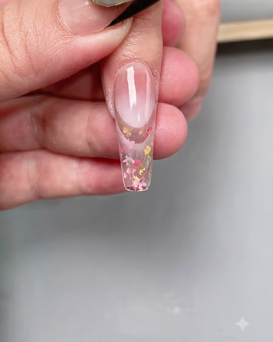ロングコフィン型の爪の先端に、細いネイルアートブラシでクリアなダイヤモンドトップコートを正確に塗っている様子。