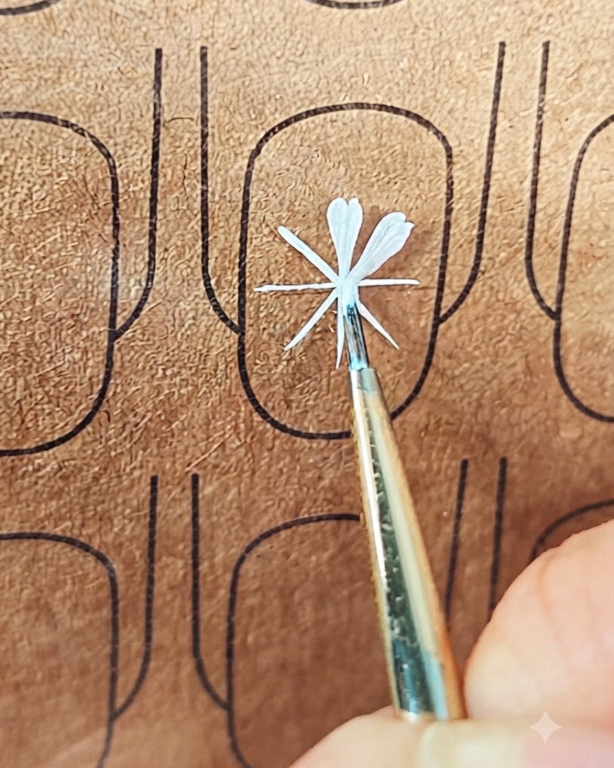 練習ボード上で2枚目の花びらを形作るために白いジェルを置いている細いネイルアートブラシ。