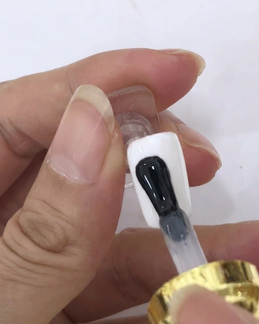 ホワイトに塗られたネイル表面に、ブラシでブルーミングジェルのクリアコートを塗布している様子。