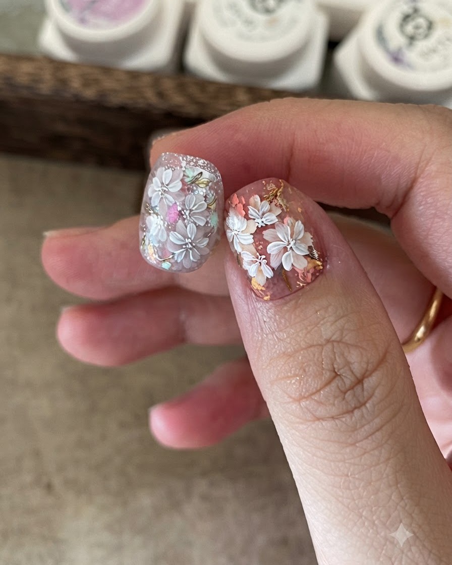 白い花のネイルアートの中心に着色ジェルを塗布するために小さなスポンジを使用しているネイルアーティストのクローズアップ。