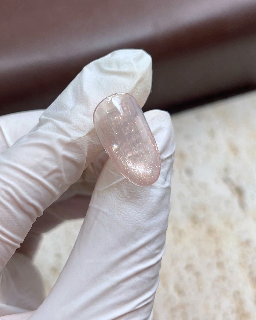 手袋をした手が、きらめくキャッツアイジェルネイルの上でマグネットスティックを持ち、パール効果を作り出している様子。