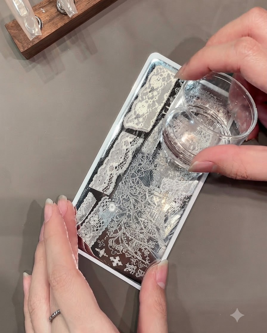 透明なジェリースタンパーが、金属製のスタンピングプレートから複雑な白いレースパターンを拾い上げている様子。