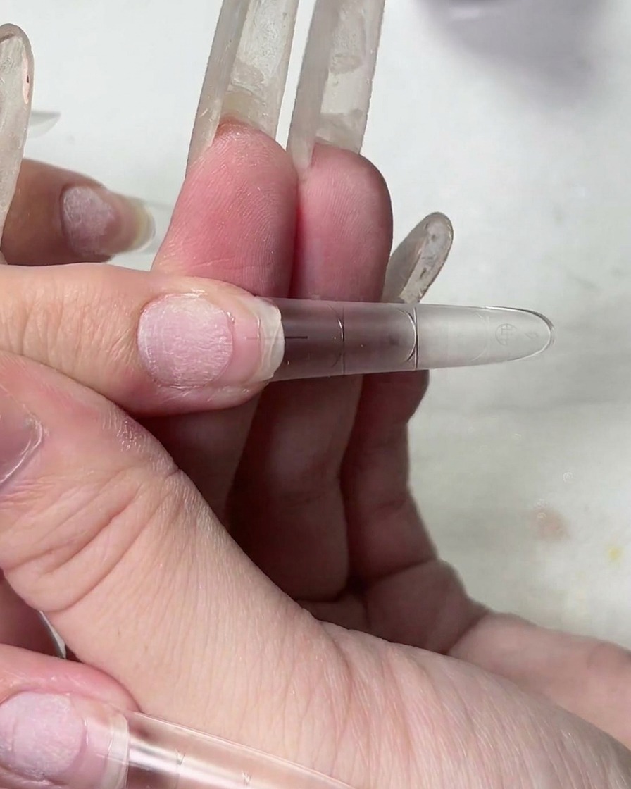 取り外したネイルチップを持ち上げ、透明な接着剤ジェルの糸を引くテクスチャーを示しているクローズアップ。
