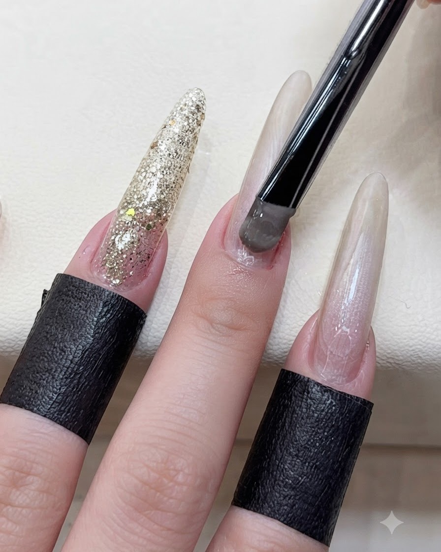 黒い柄のブラシを使い、長さ出しをした指のネイルベッドにグレーブラウンのキャッツアイジェルを塗布しているクローズアップ画像。