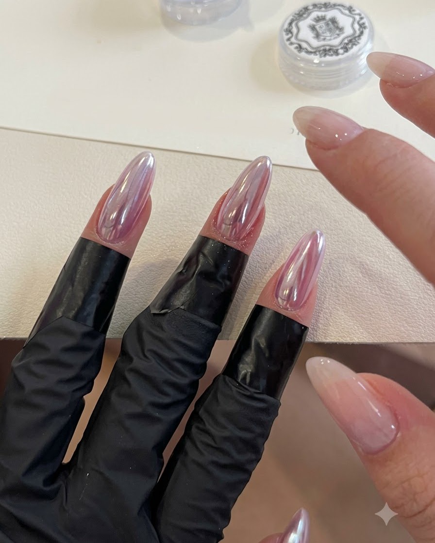 スポンジアプリケーターを使って、アーモンドシェイプのクロームネイルに虹色のスカイミラーパウダーをバッフィングしている様子。