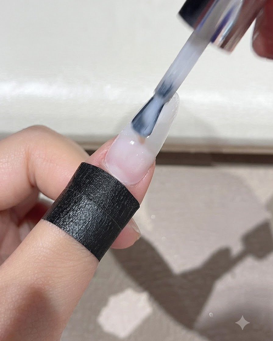 ブラシを使用して、ミルキーホワイトのセルフレベリングジェルをネイルの表面全体に均一に広げている様子。