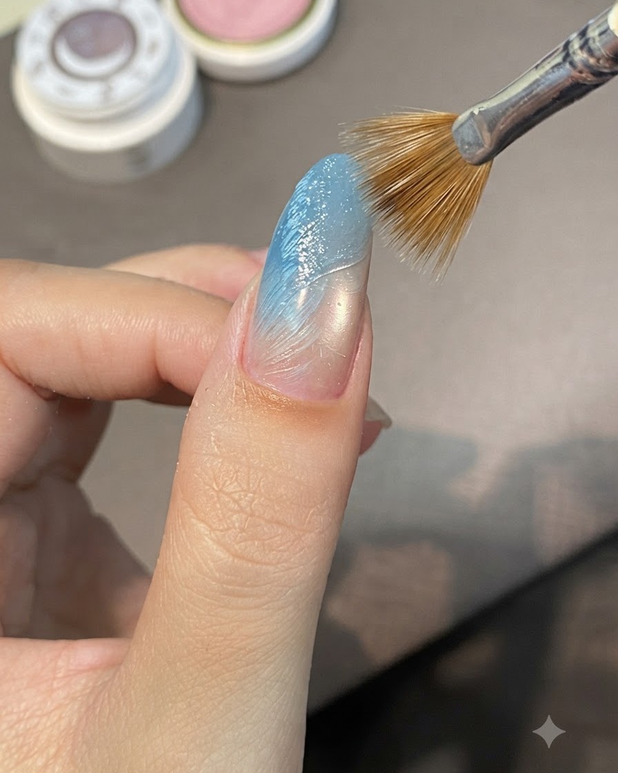 ブルーのグラデーションネイル上の未硬化のスカルプチュアジェルを、細筆を使って斜めに掃くように動かし、盛り上がった畝を作っている様子。