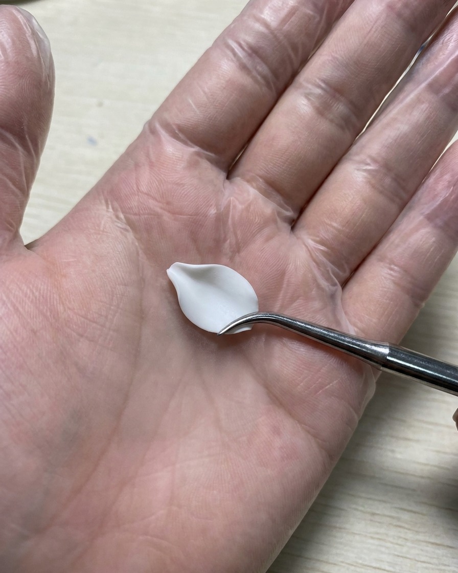 手袋をした手でシリコン製のカービングツールを持ち、シリコンマットの上に置かれた白い3Dジェルの花びらをなめらかに整えている様子。