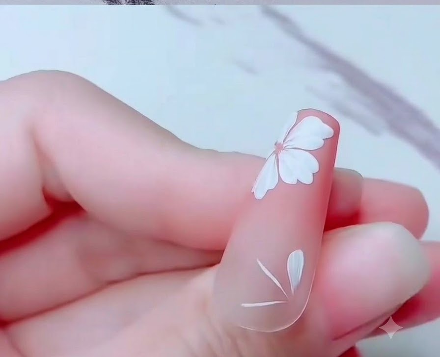爪の根元付近に描かれた、白い桜の花びらの一部を示すネイルのアップ。