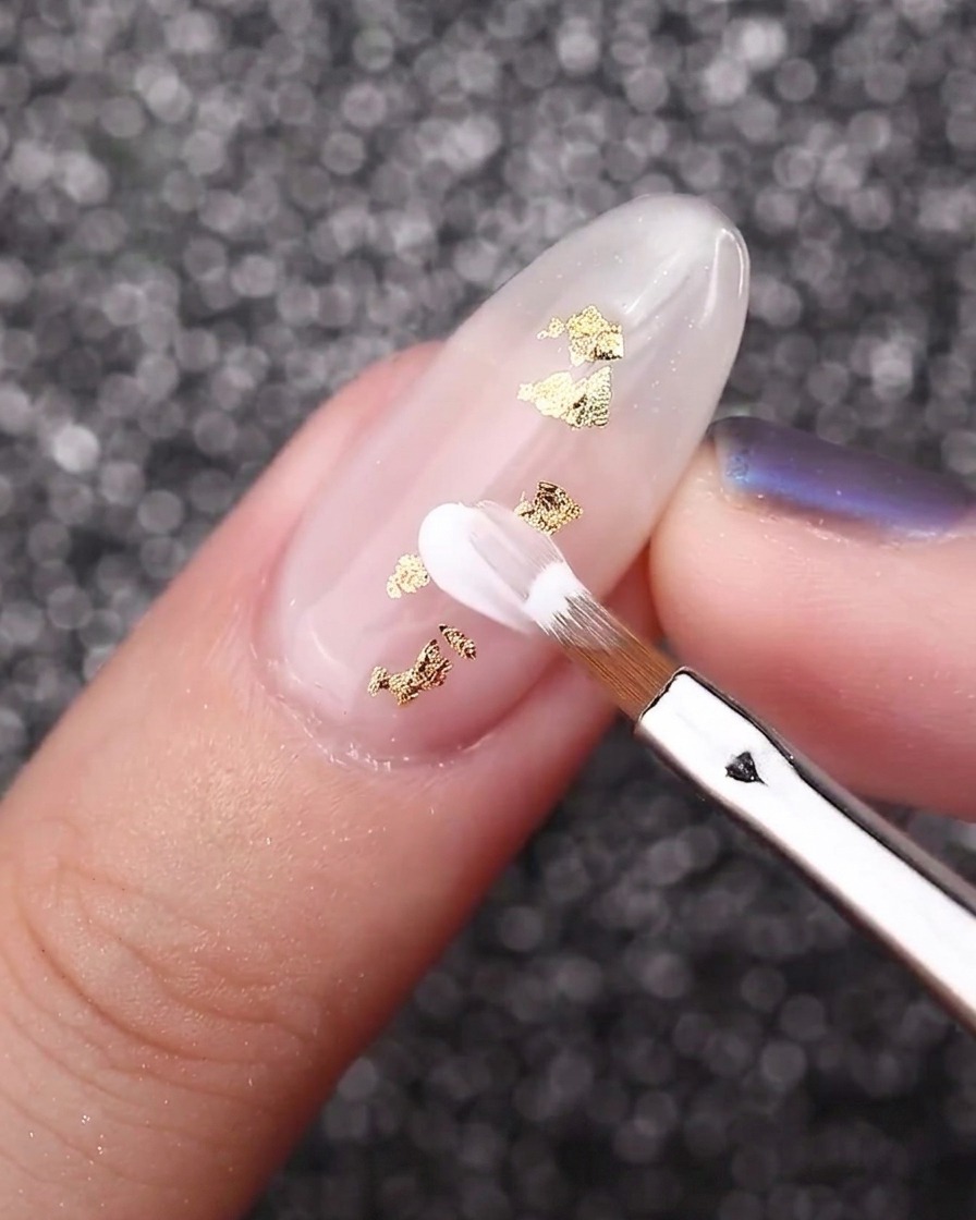 金箔のアクセントが入ったミルキーホワイトの爪に、斜めカットのブラシで白い花びらを描いている様子。