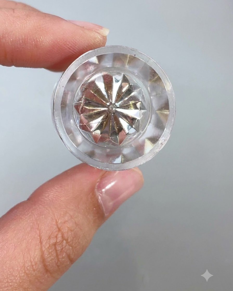 明るい背景を背に、光を反射するクリアな多面体クリスタルの容器の蓋またはアプリケーターツールのクローズアップ。