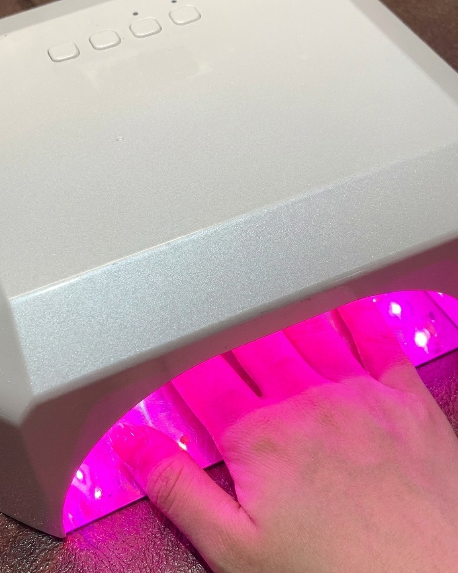 硬化中にピンク色の光を放つ標準的な大型UV/LEDネイルランプの中に手が入れられている様子。