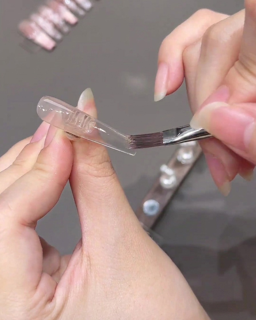 ネイルチップに塗ったピンクジェルの境界線をフラットブラシで優しくぼかす様子。
