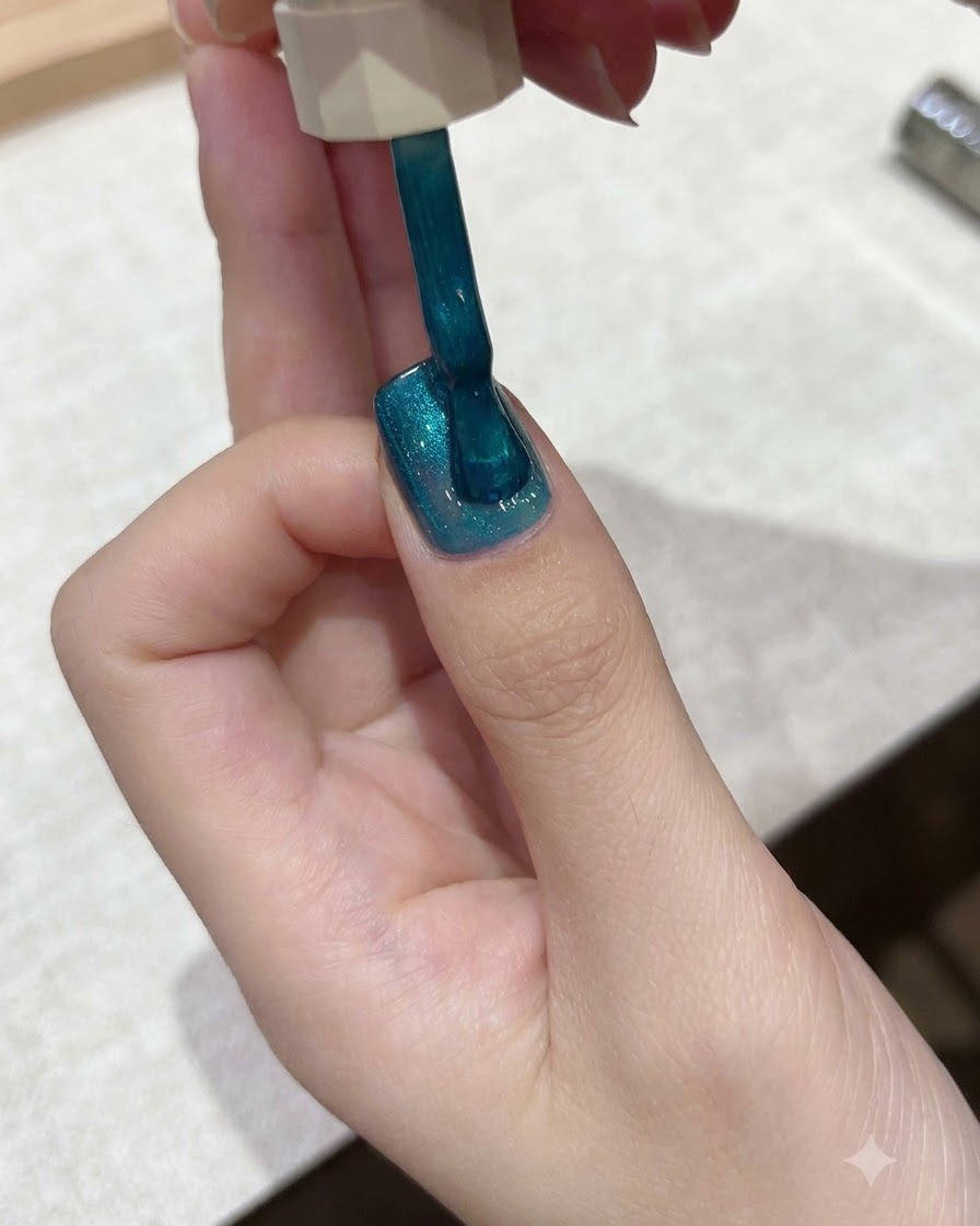 爪の表面全体に、鮮やかなティールブルーのキャッツアイジェルポリッシュをブラシで塗布している様子。