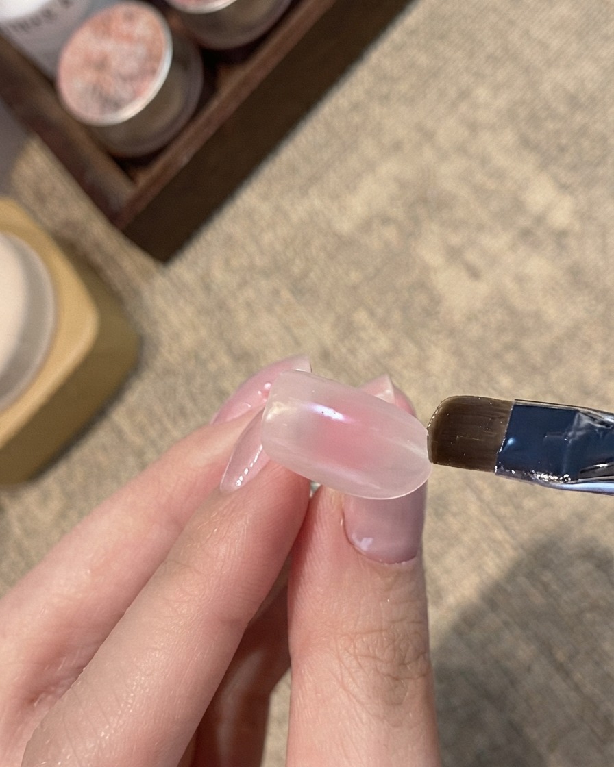 ピンクがかったヌードネイルの先端にブルーシマーのキャッツアイジェルをフラットブラシで塗布している様子。