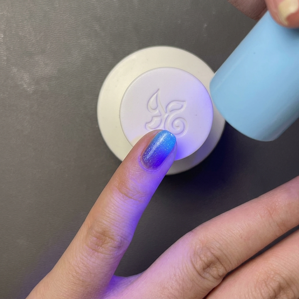 明るいブルーのジェルポリッシュを塗った指を、小型で手持ちタイプのライトブルーのUV/LEDランプで硬化させている様子。