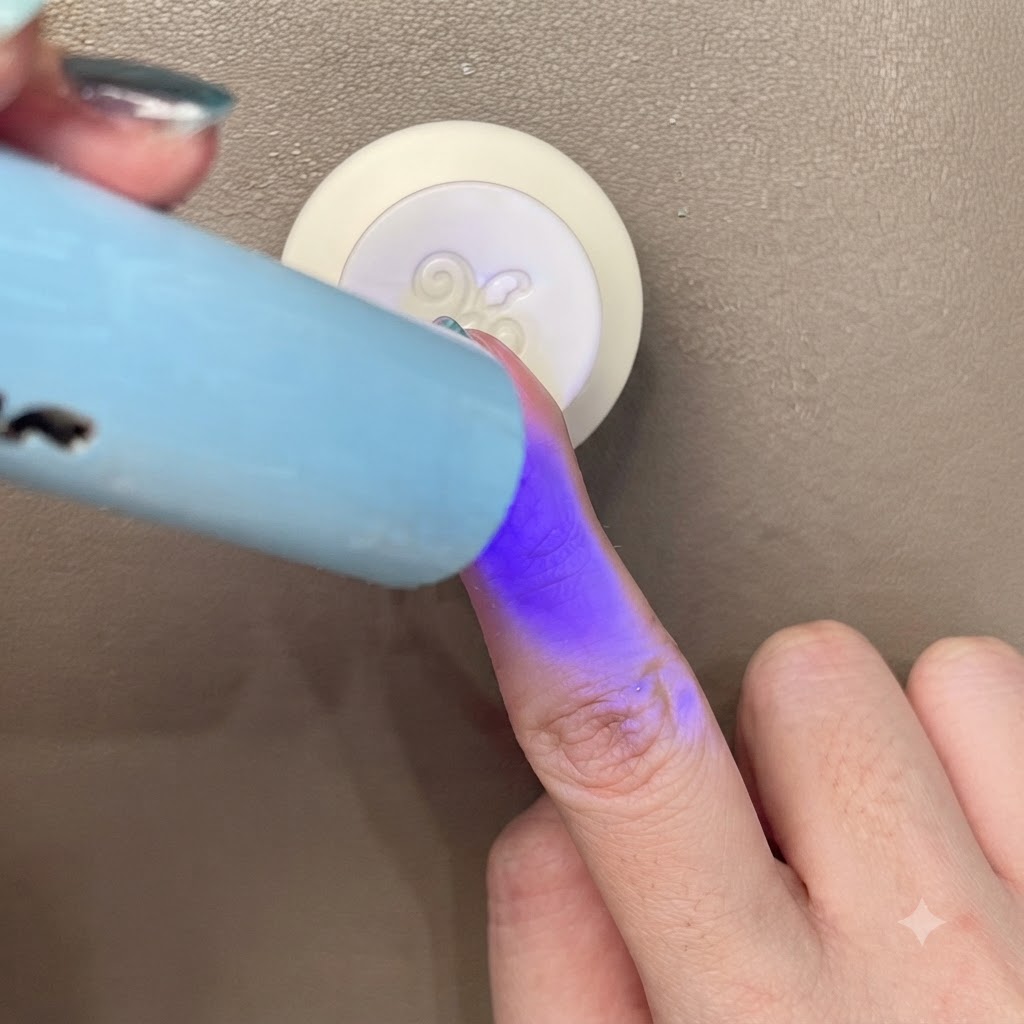 ブルーグリーンのキャッツアイネイルを、小型のポータブルな青いUV/LEDライトで硬化させている様子。