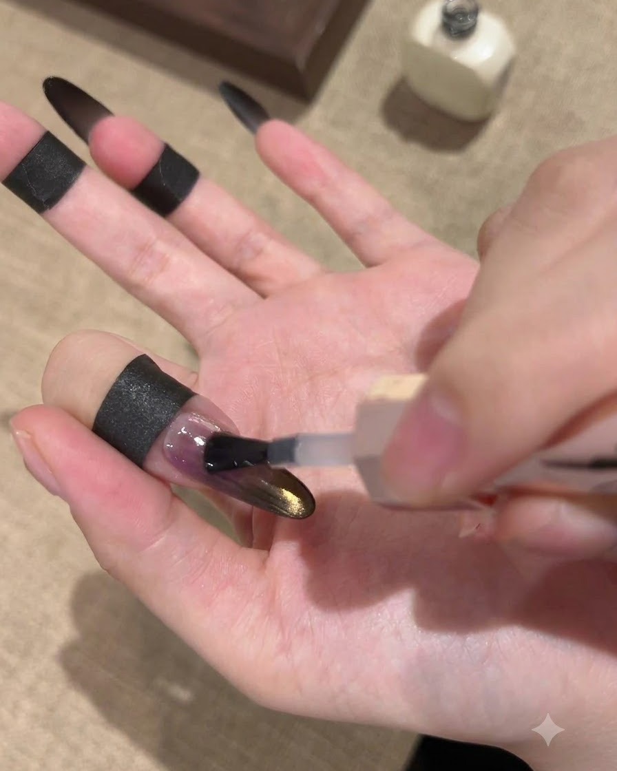 ブラックとゴールドのグラデーションキャッツアイネイルの上に、ブラシで艶やかなシーリングトップコートを塗布している様子。