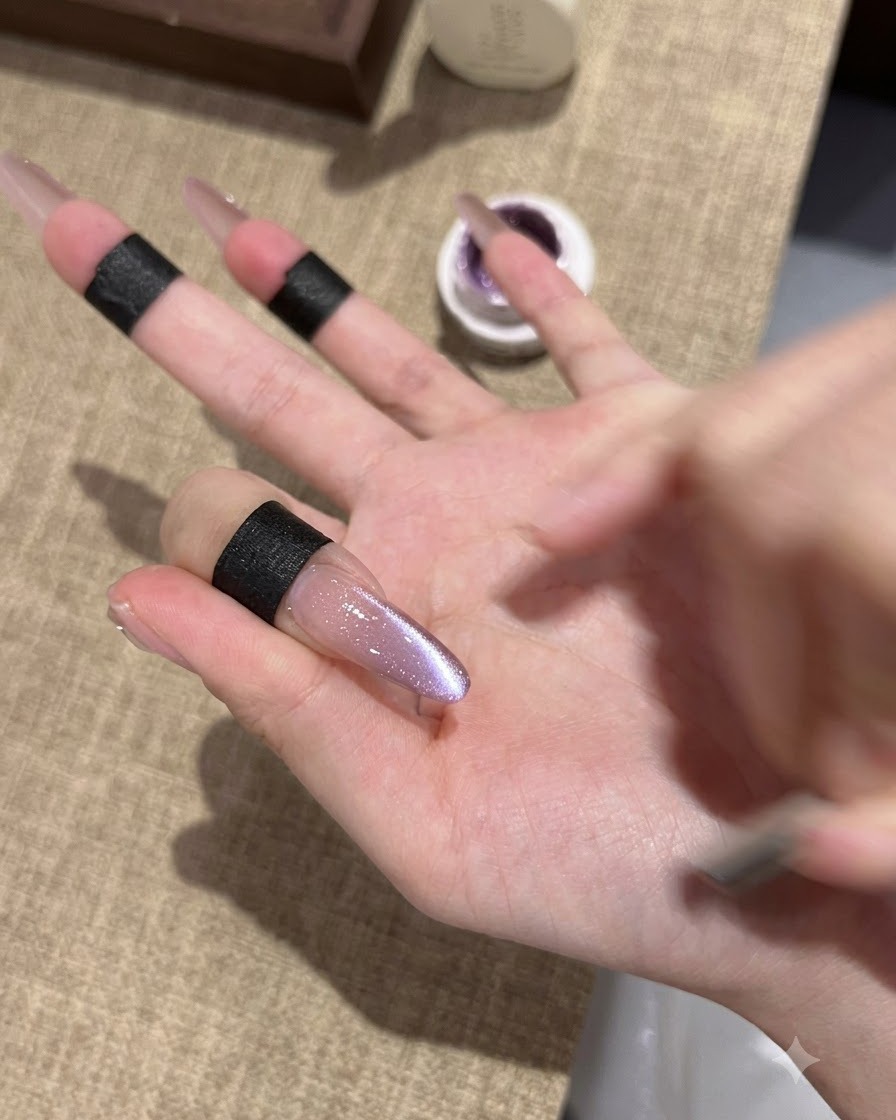 キラキラと反射する中央のラインが特徴的な、塗りたてのパープルキャッツアイジェルが施されたアーモンド型ロングネイルのアップ。