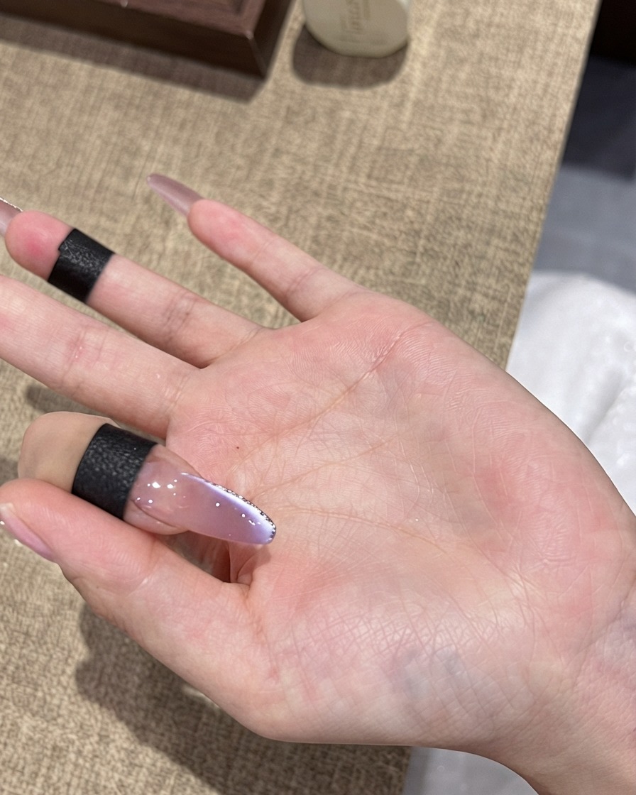 極細のシルバーラメの縁取りが施されたパープルのオンブレキャッツアイネイルの上に、仕上げの艶やかなトップコートをブラシで塗る様子。