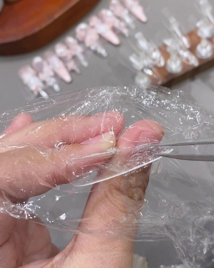 硬化してテクスチャーができた透明なネイルチップから、ピンセットでラップフィルムを剥がす様子。