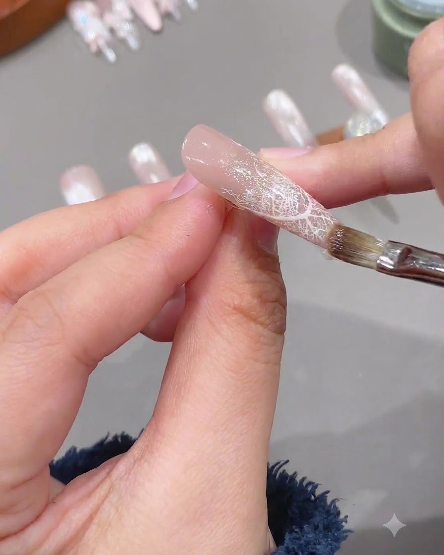 レースデザインが施された爪の上に、透明なソフト補強ジェルをブラシで塗る様子。