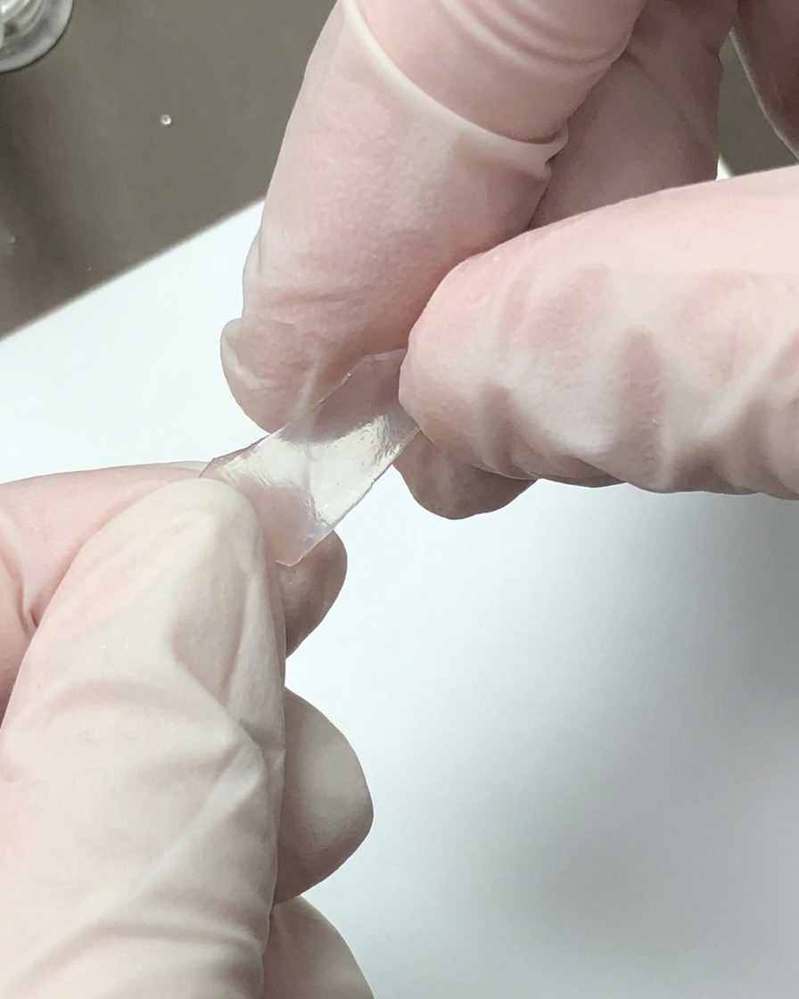 手袋を着用した両手が、半透明の装飾シートを手で小さな破片に砕いている様子。