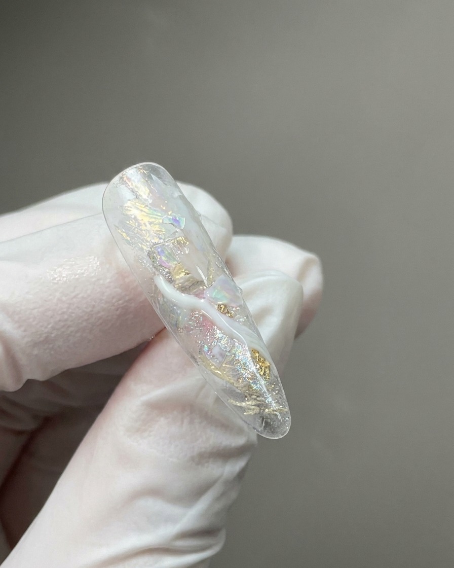 埋め込まれたシマーフレークとミルキーホワイトの大理石風の繊細な筋が特徴のクリアなネイルチップのクローズアップ。