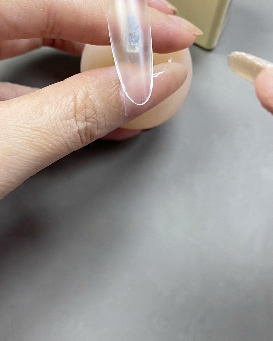 クリアネイルエクステンションの上にベースジェルのクリア層をブラシで塗布している様子。