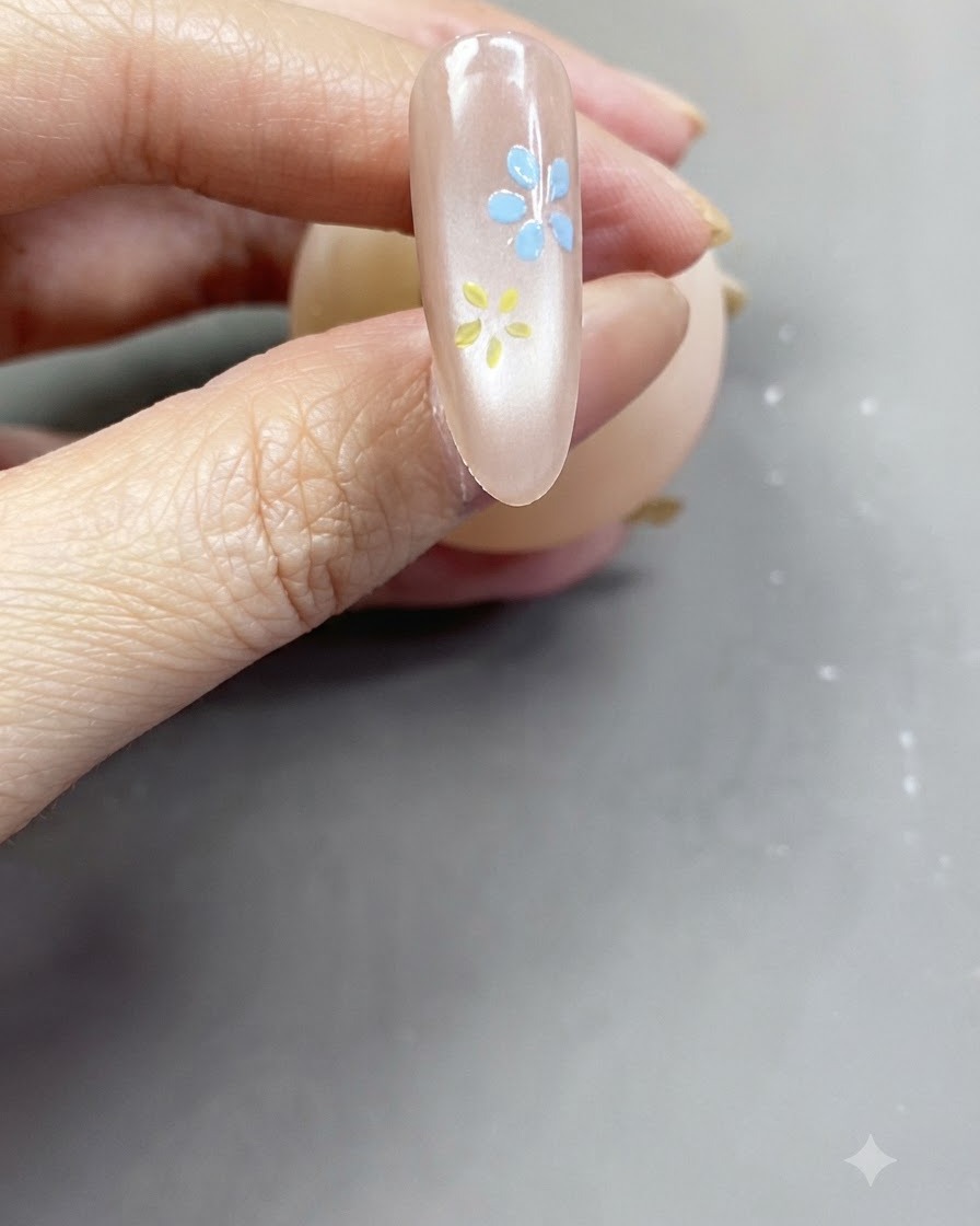 光沢のあるヌードピンクのネイルの上に描かれた、完成したソフトピンクの花のクローズアップビュー。