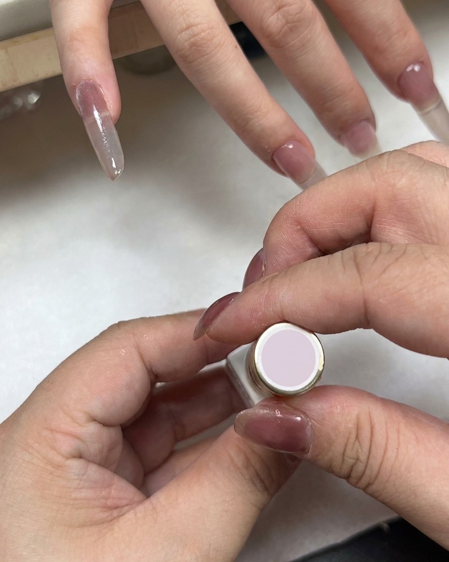 手の近くにある薄ピンクのキャップのネイルボトルと、グラデーションが施された爪。