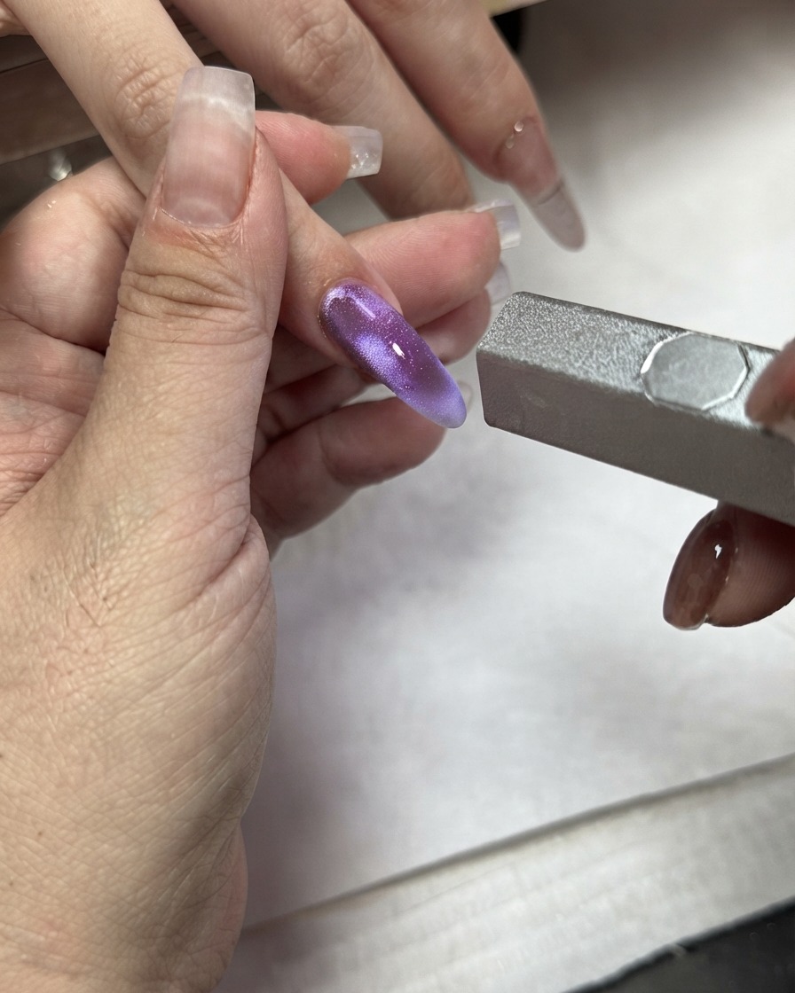 人差し指に塗ったパープルのキャッツアイジェルにマグネットスティックを当てている様子。