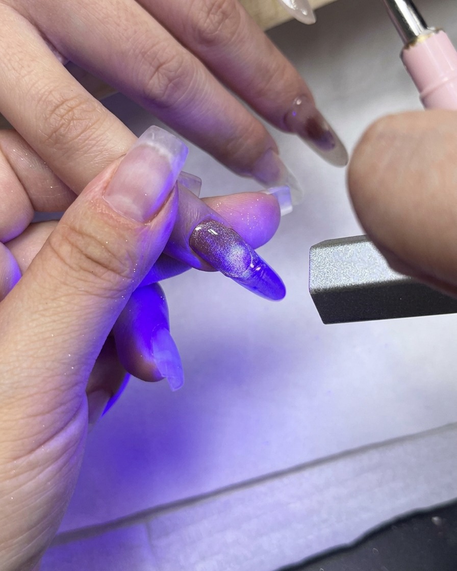 凹凸のあるフレンチラインが施された中指に、直接UV/LEDライトを当てて硬化している様子。