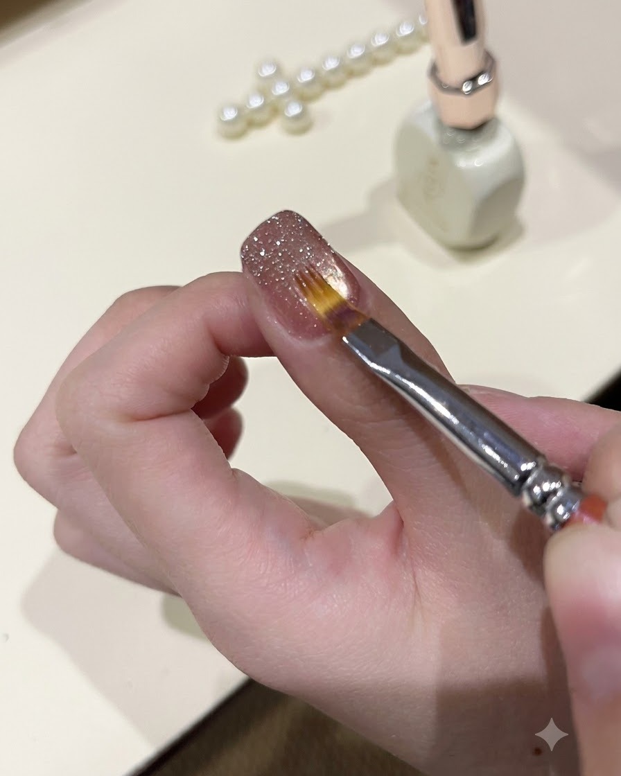 マニキュアを施した爪の表面で、極細ブラシを使ってキラキラしたグリッタージェルを滑らかに整えている様子。