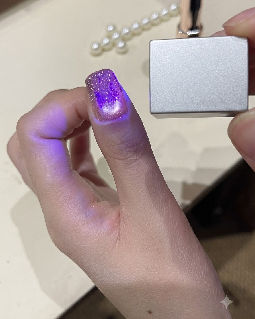 小型のハンディUV LEDライトの下で親指を照らし、ジェルポリッシュを硬化させているクローズアップビュー。