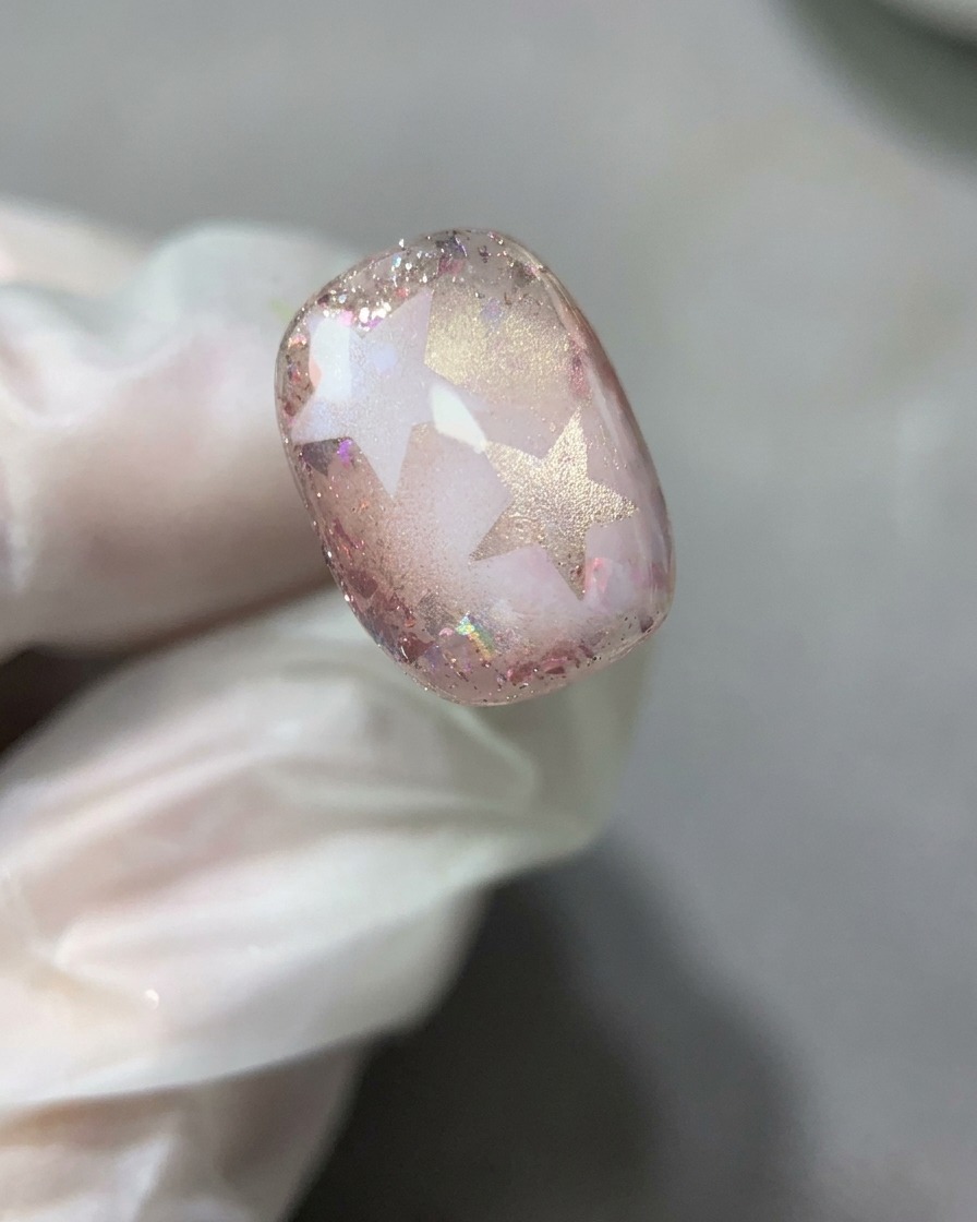 完成した星とグリッターのネイルデザインの上に、クリアなベースジェルを滑らかで薄い層として広げているネイルブラシの様子。