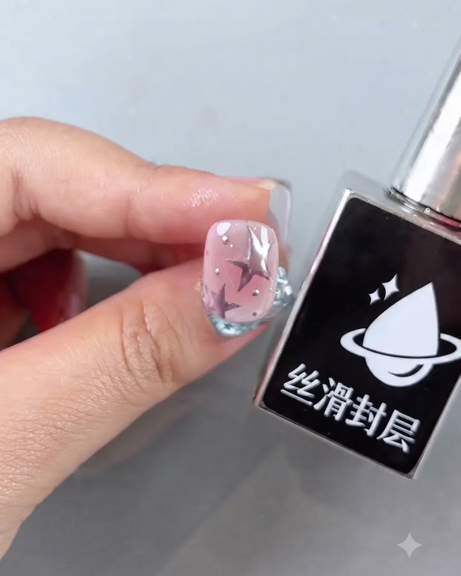 星のデザインと輝くシルバーのアクセントが施された完成したピンクの爪の横にあるスムーズトップコートのボトル。