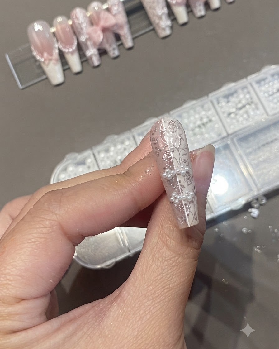 パールとレースのスタンプを特徴とするテクスチャードネイルデザインの上にクリアトップコートを塗布しているネイルブラシ。
