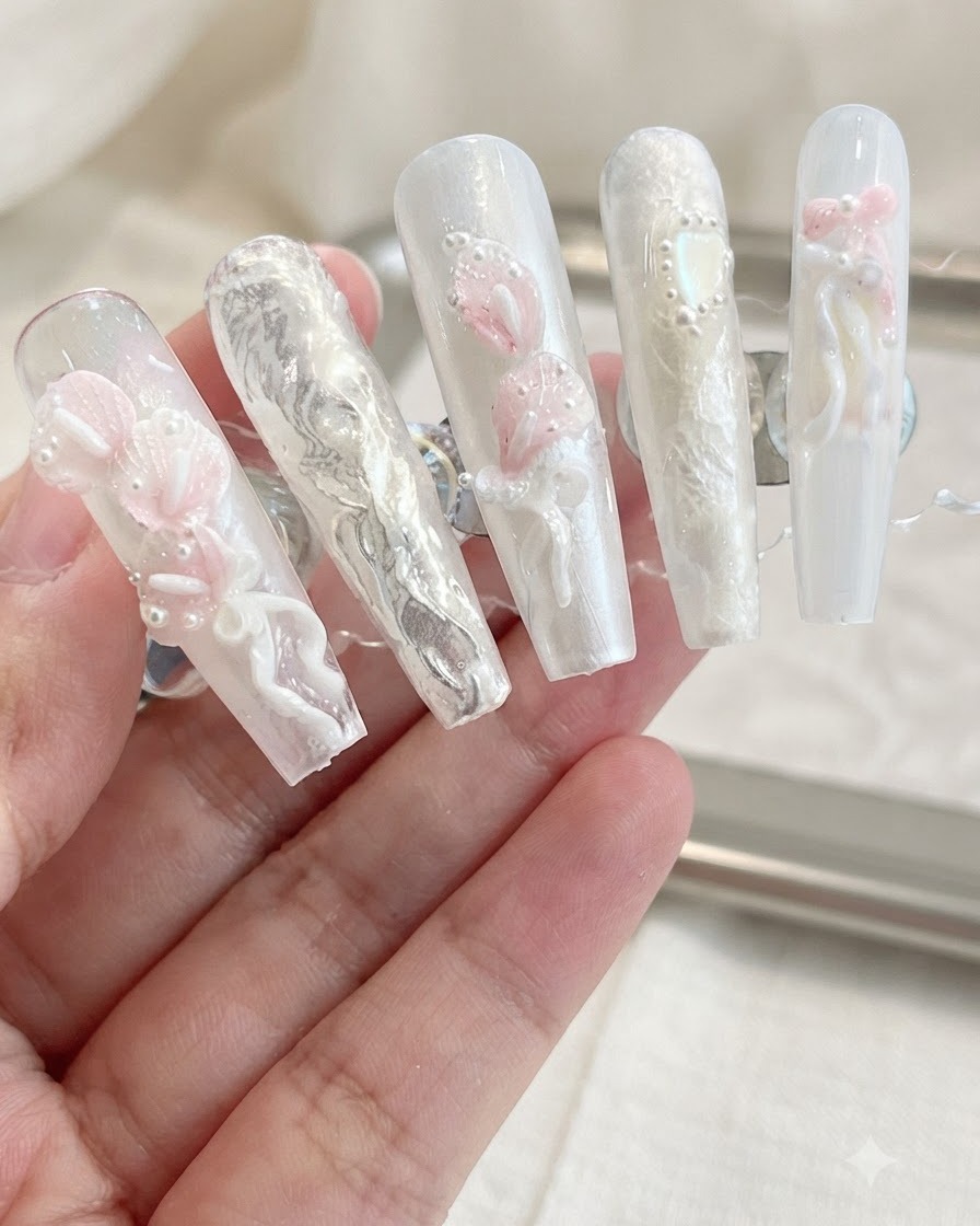 ニュートラルな背景の上で、3Dカラーリリー、リボン、パールの装飾が施された完成したネイルチップのディスプレイ。